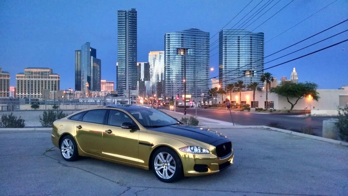 Gold chrome wrapped Jaguar XJ at dusk with the Las Vegas Strip skyline behind it